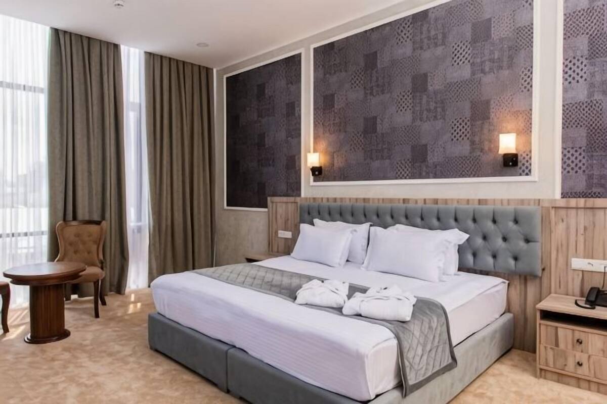 Una habitación de hotel con una cama grande, una silla, una mesita pequeña y una mesita de noche.