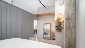 A bedroom with a large bed, a wooden ceiling, a wall-mounted hat rack, and a view of a dining area.