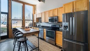 A modern kitchen with wooden cabinets, stainless steel appliances, and a dining area with stools.
