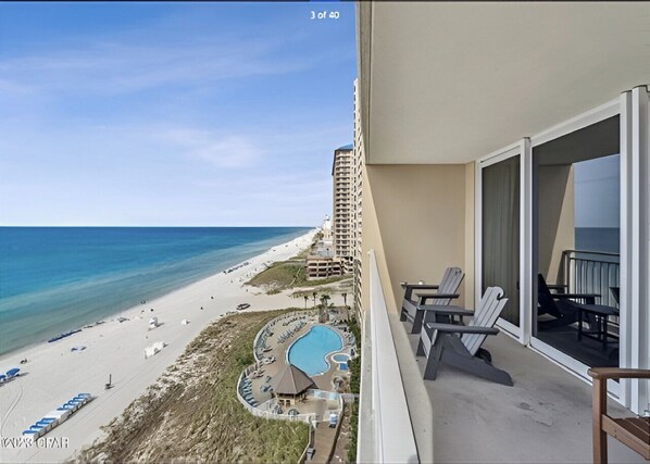Un balcon avec vue sur une plage, une piscine et un immeuble.