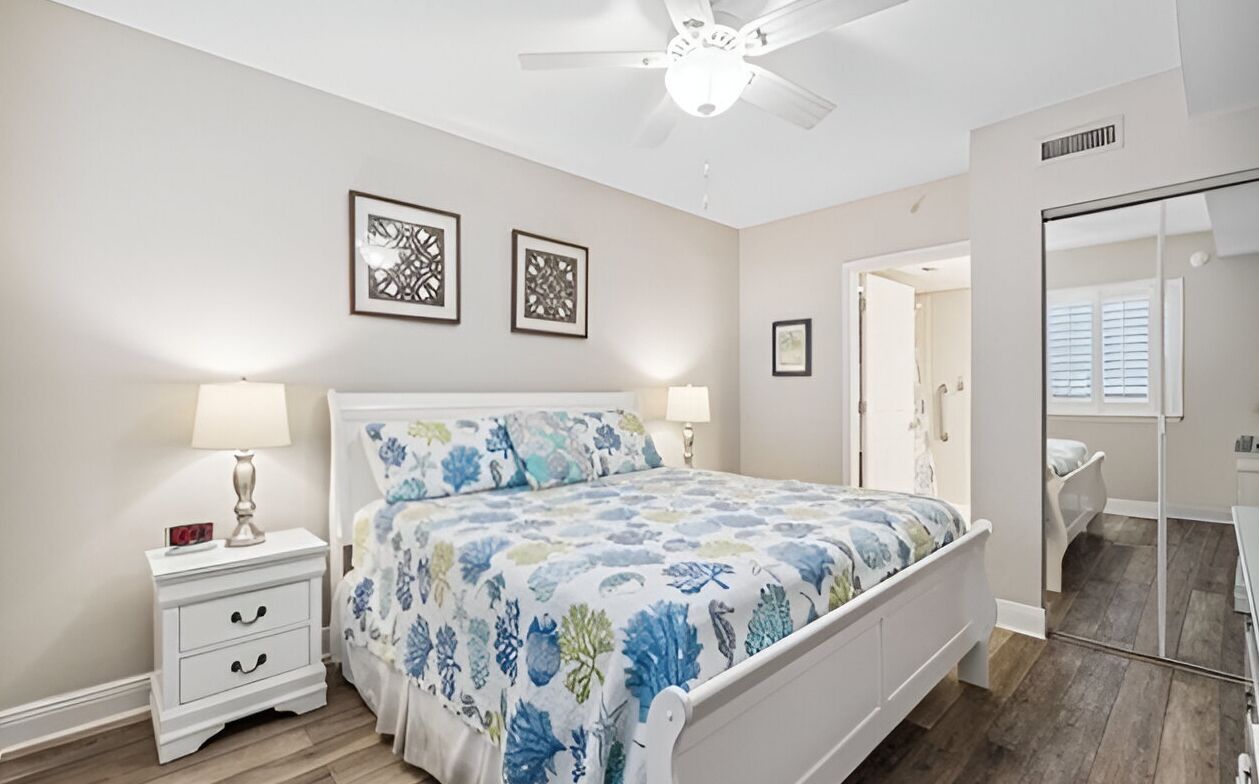 A bedroom with a bed, nightstands, a ceiling fan, and framed artwork on the wall.