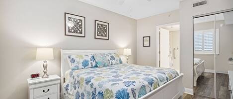 A bedroom with a bed, nightstands, a ceiling fan, and framed artwork on the wall.