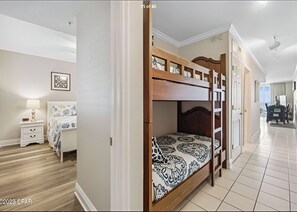Une chambre avec un lit superposé, une table de chevet, une lampe et un tableau encadré au mur.