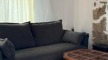 Una habitación con un sofá de color gris oscuro, una mesa de centro de madera con motivos y un suelo de baldosas.