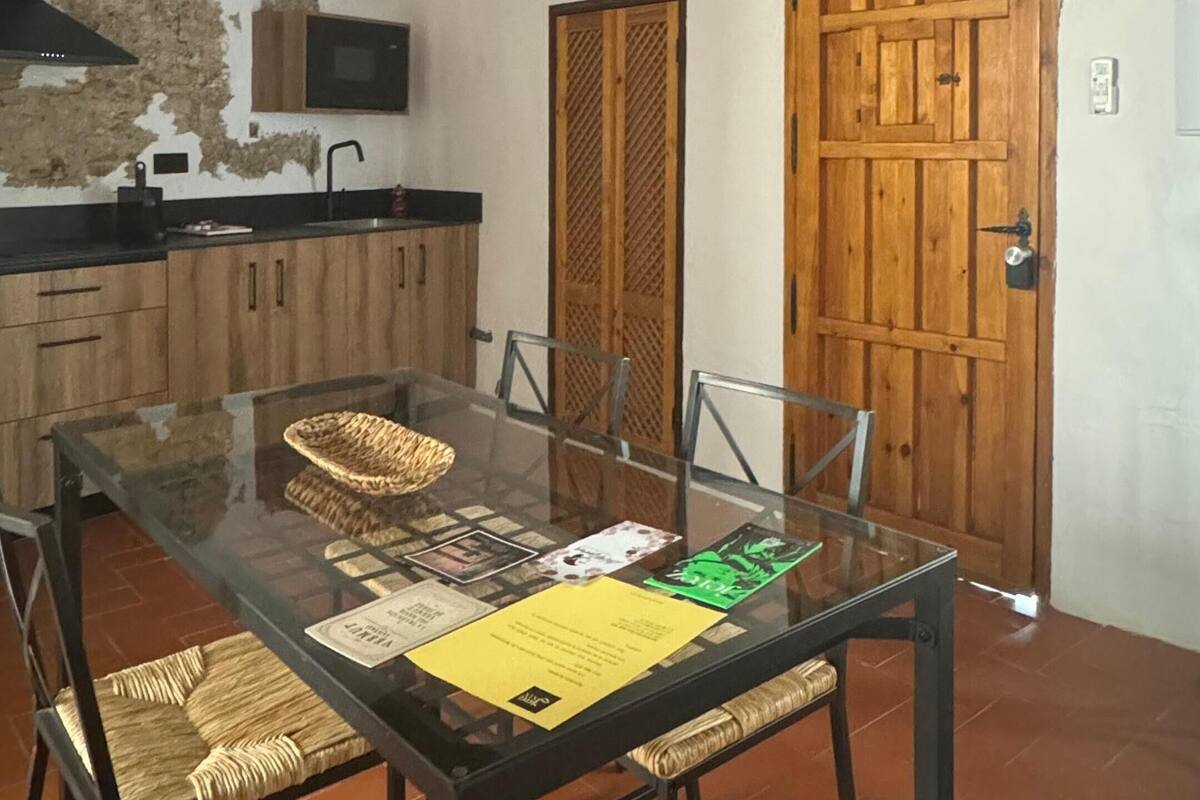 Un coin repas avec une table en verre, des chaises en osier, un mur en pierre et une porte en bois.