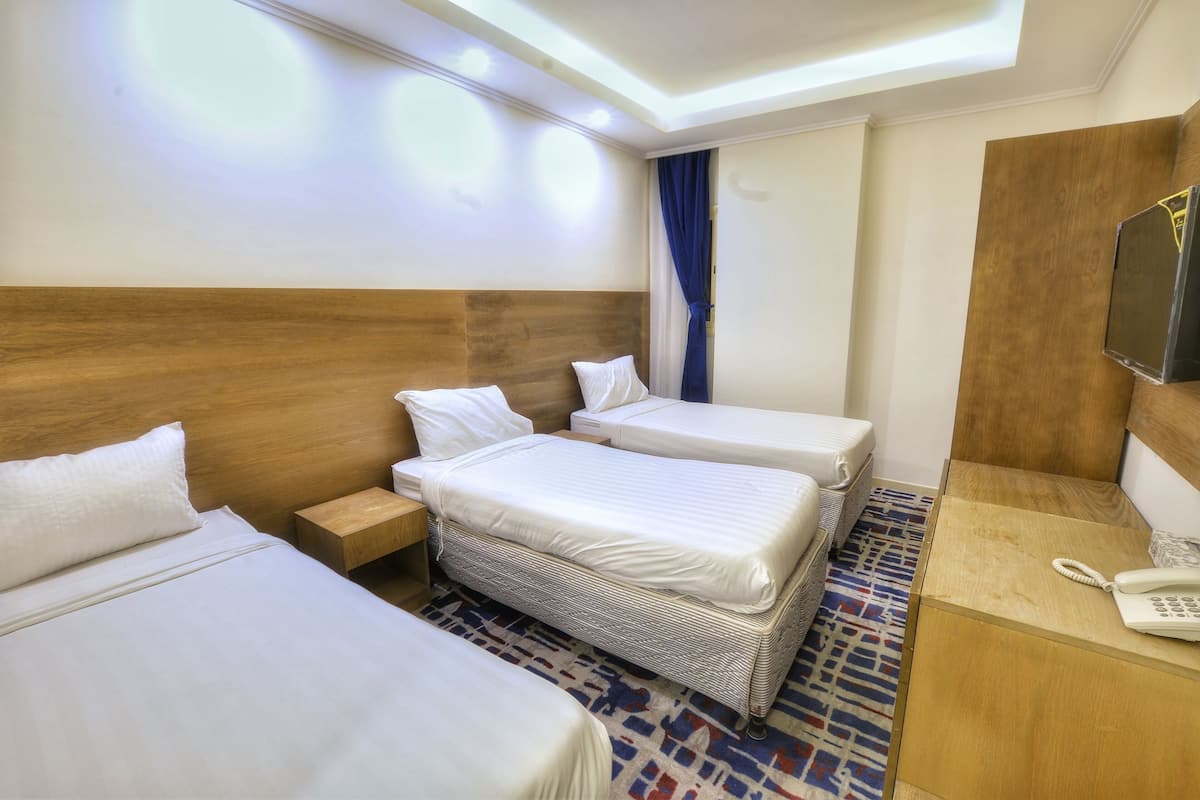 A hotel room with two beds, a wooden headboard, a small bedside table with a lamp, a telephone, and a television on a wooden cabinet.