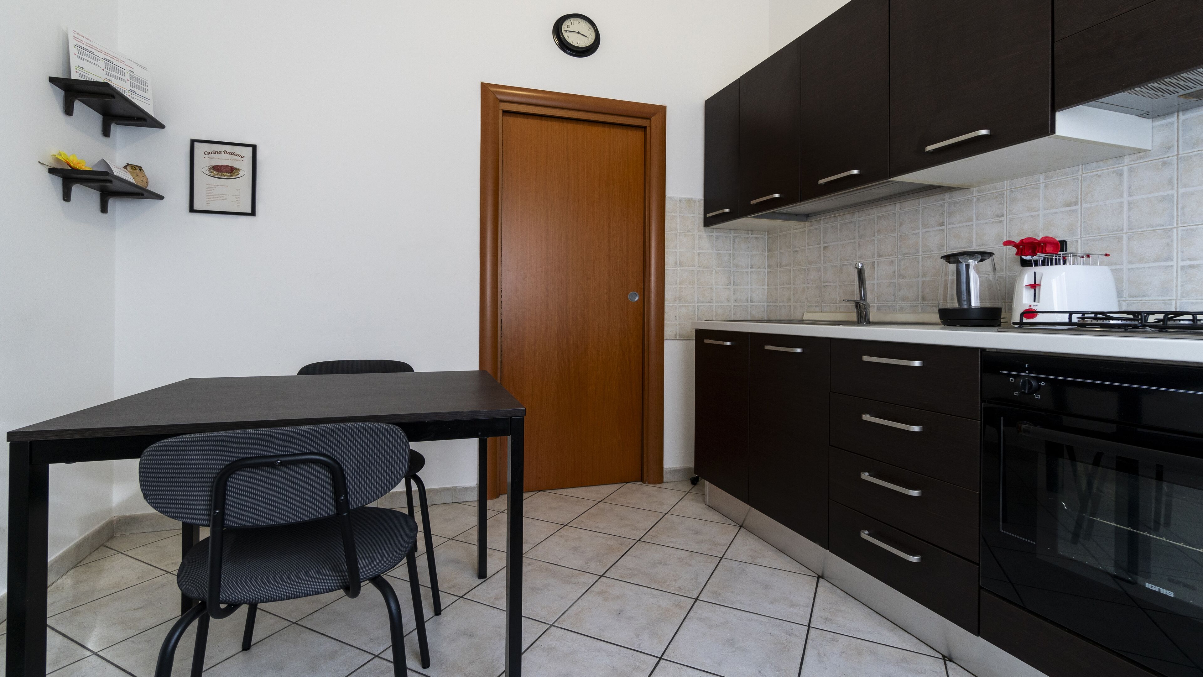 A compact kitchen with dark cabinets, a wooden door, a tiled backsplash, and a stove.