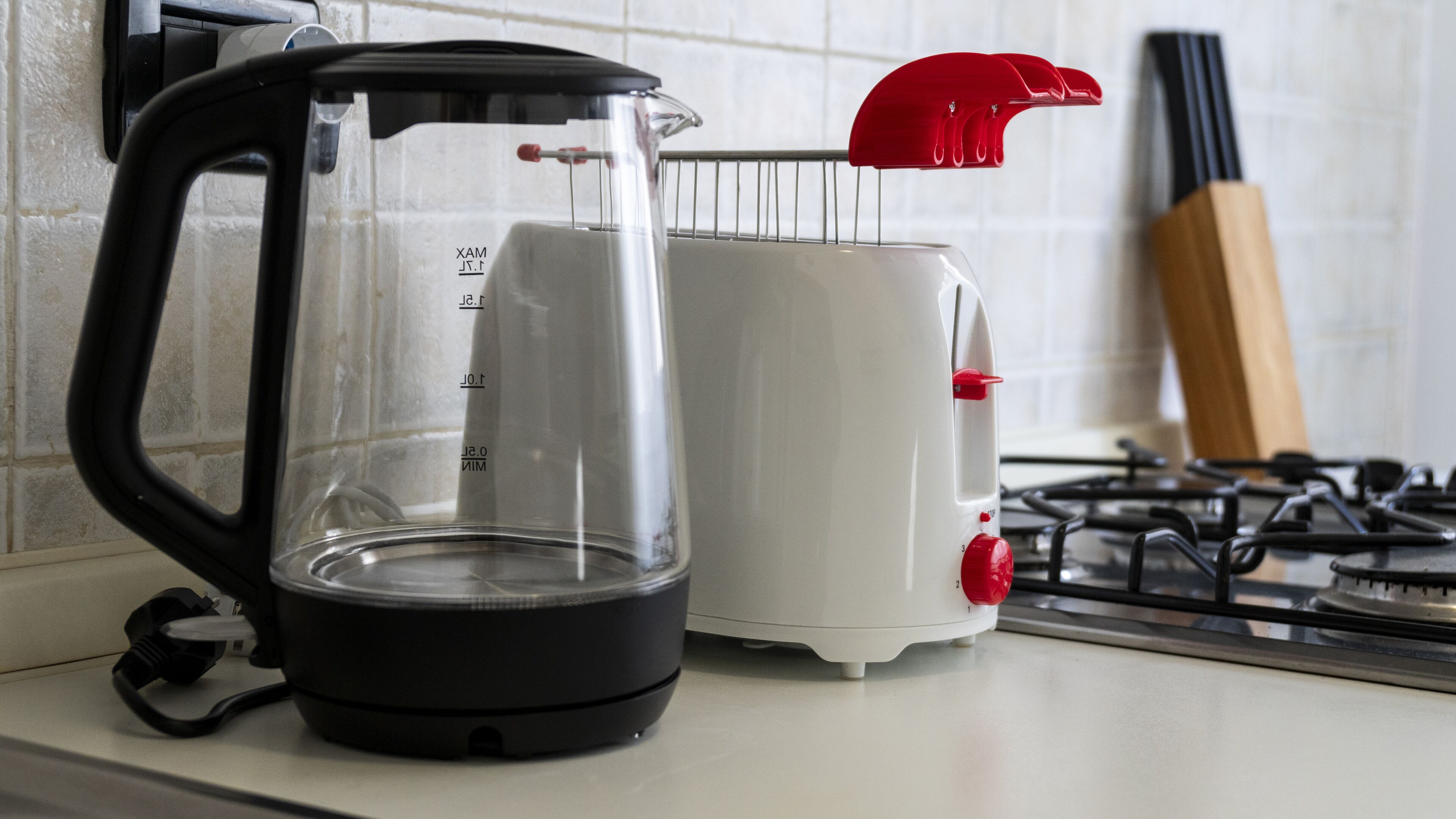 A kitchen with a black electric kettle, a white toaster, and a gas stove.