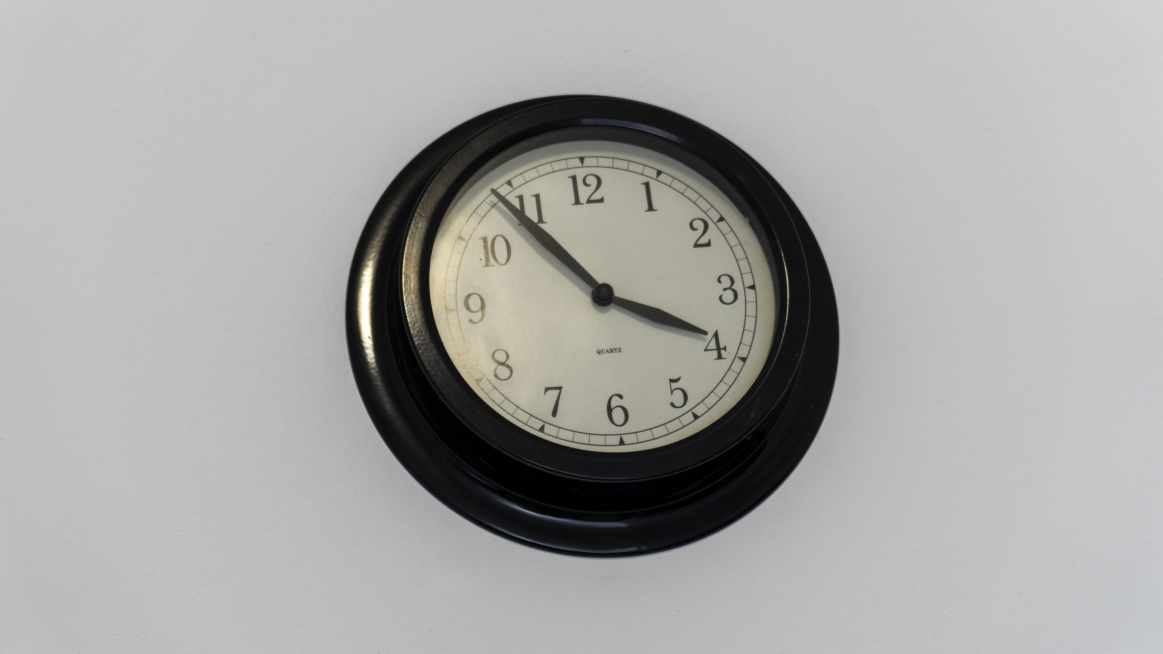 Orologio da parete rotondo con cornice nera e quadrante bianco, che segna circa le 3:50.