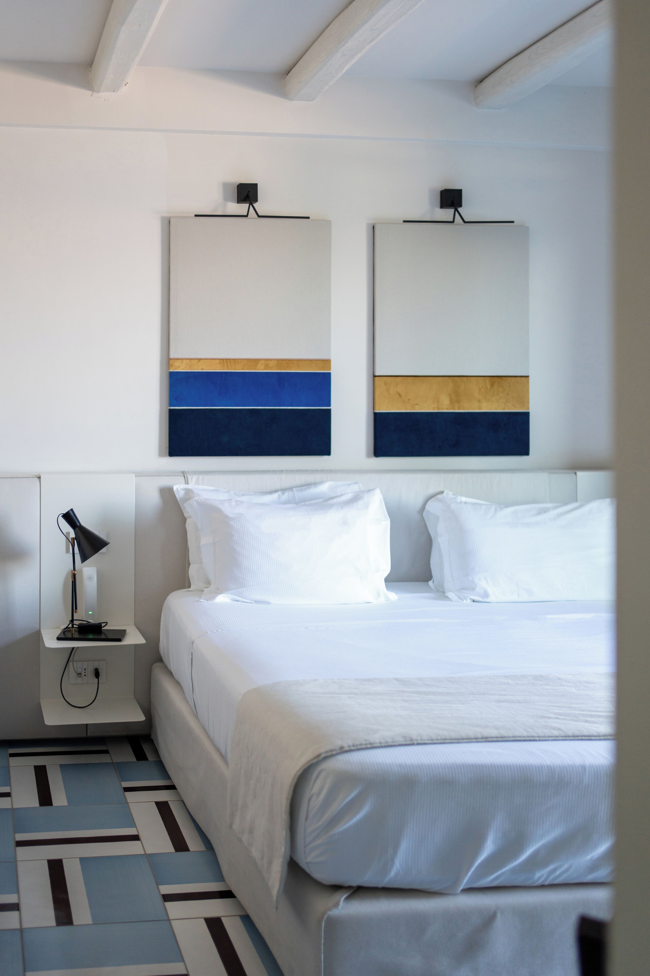 Une chambre d’hôtel avec un lit, une table de chevet avec une lampe et une œuvre d’art abstraite au mur.