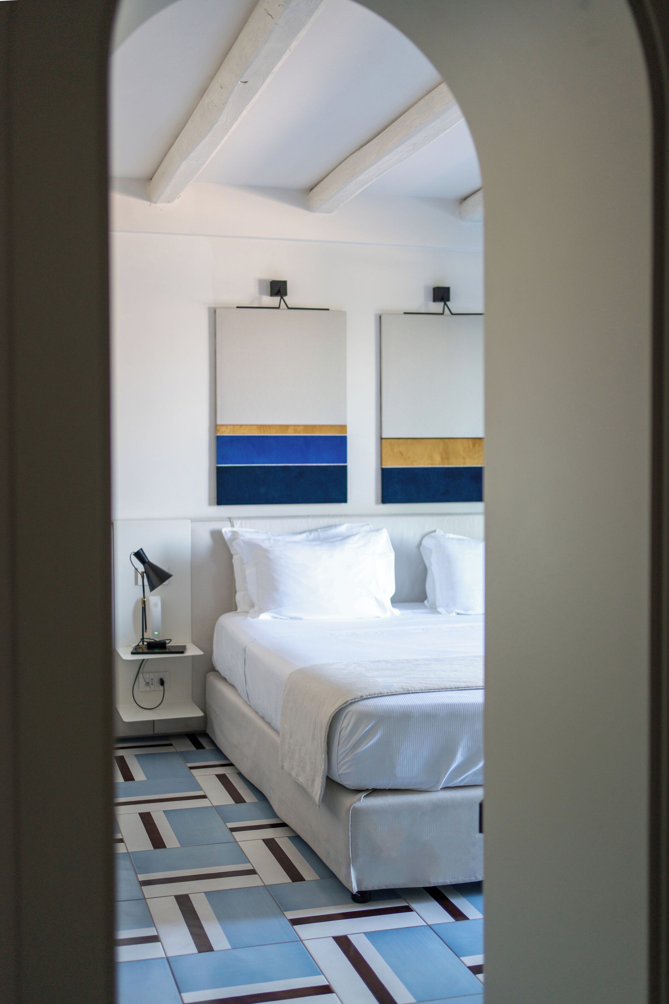 A hotel room with a bed, a nightstand, a lamp, and a wall with abstract art.