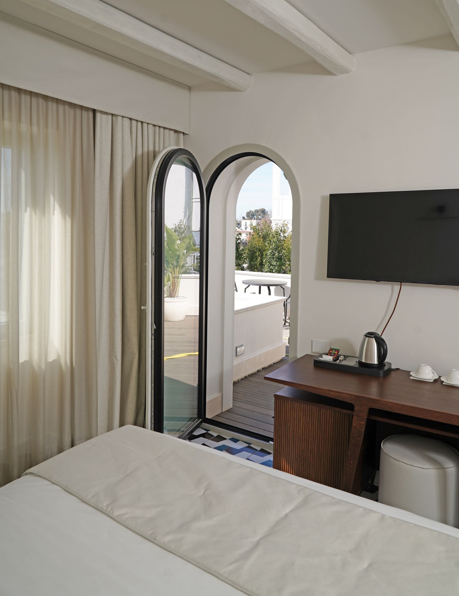 Ein Hotelzimmer mit einem Bett, einem Schreibtisch mit Kaffeemaschine, einem Fernseher und einer Glastür, die zu einem Außenbereich führt.