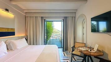 Habitación de hotel con una cama grande, un escritorio con una silla, un televisor y vistas a un patio exterior.