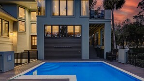 A modern two-story house with a swimming pool, a covered patio, and a view of the sunset.