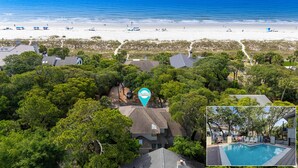 An aerial view of a residential area with a beach, dense greenery, and a swimming pool.