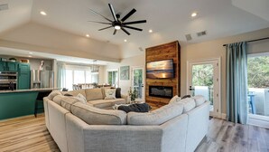 A modern living room with a large sectional sofa, a fireplace, and a television mounted on a wooden wall.