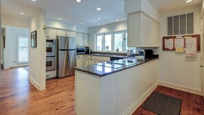 A modern kitchen with white cabinetry, stainless steel appliances, a granite countertop, and a large window providing natural light. - 2 Duck Hawk - Sea Pines just a Short Walk to the Beach & Private Pool (Hilton Head Island)