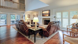 A spacious living room with a fireplace, leather sofas, and a high ceiling with a balcony. - 2 Duck Hawk - Sea Pines just a Short Walk to the Beach & Private Pool (Hilton Head Island)