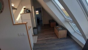 A narrow, sloped hallway with wooden flooring, a small wooden bench, and a window on the right. - Ferienwohnung "weit Blick" (Dornum)