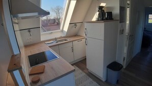 A compact kitchen with a window, a sink, a coffee maker, and a trash bin. - Ferienwohnung "weit Blick" (Dornum)