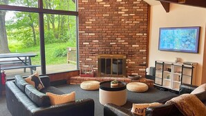 Ein gemütliches Wohnzimmer mit Kamin aus Ziegelsteinen, Ledersofas und einem großen Fenster mit Blick auf einen Garten.