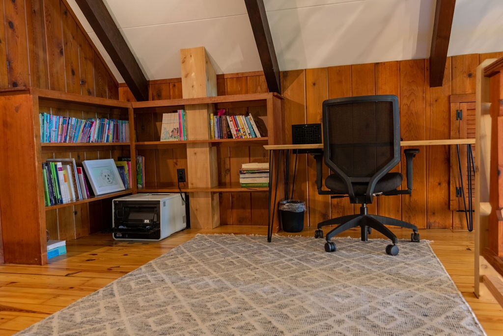 Ein Zimmer mit Holzwänden und -decke, einem Bücherregal voller Bücher, einem Schreibtisch mit einem Computer und einem Stuhl.
