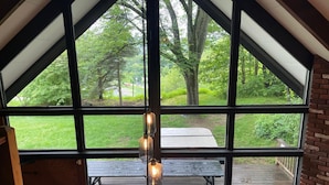 Ein Zimmer mit großen Fenstern, die auf eine Holzterrasse und einen Picknicktisch blicken.