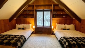 Ein gemütliches Schlafzimmer unter dem Dach mit zwei Betten, Holzbalken, einem großen Fenster und einer Hängeleuchte.