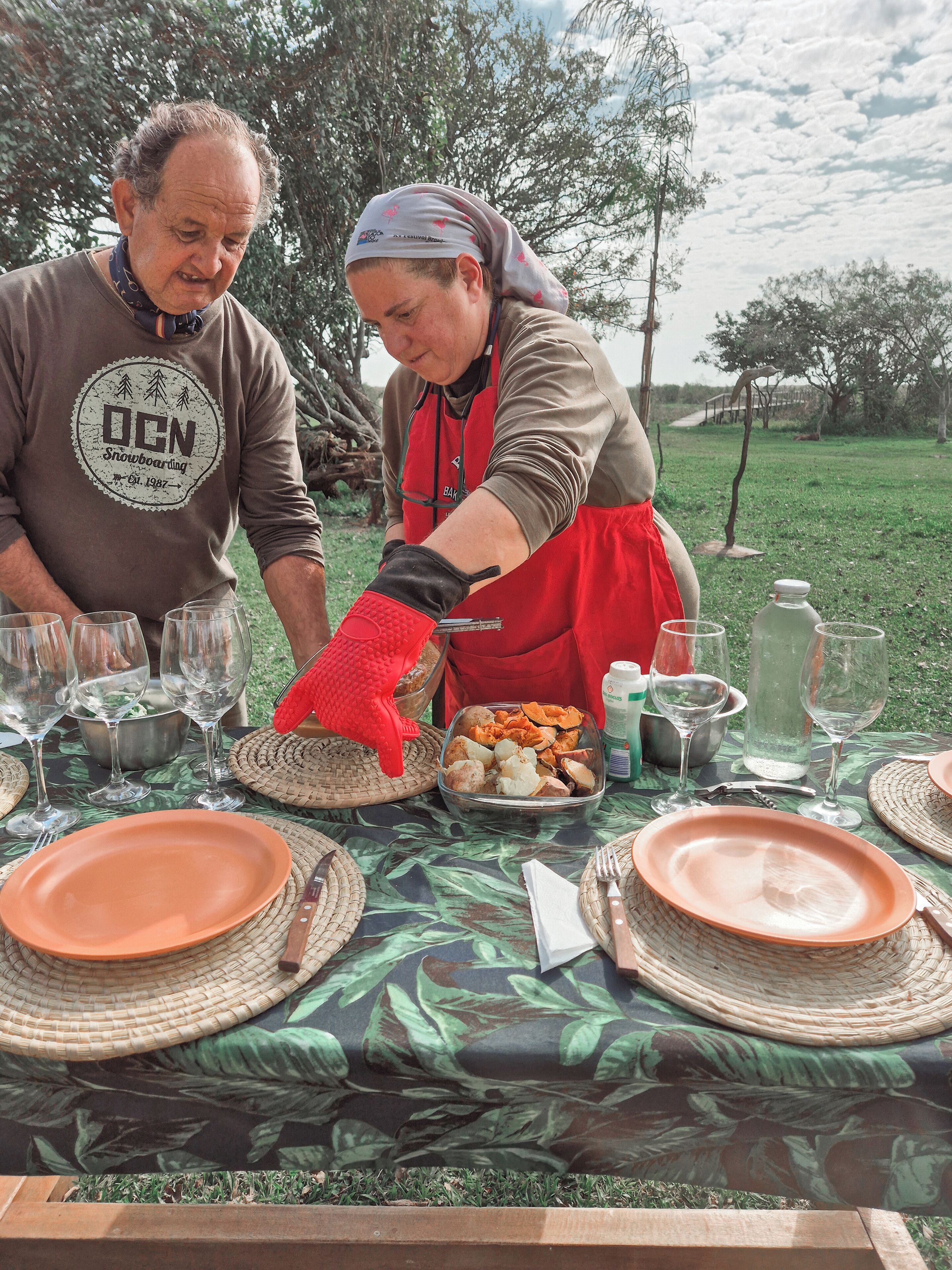 Une table dressée à l’extérieur, avec des assiettes, des verres et un plat rempli de nourriture.