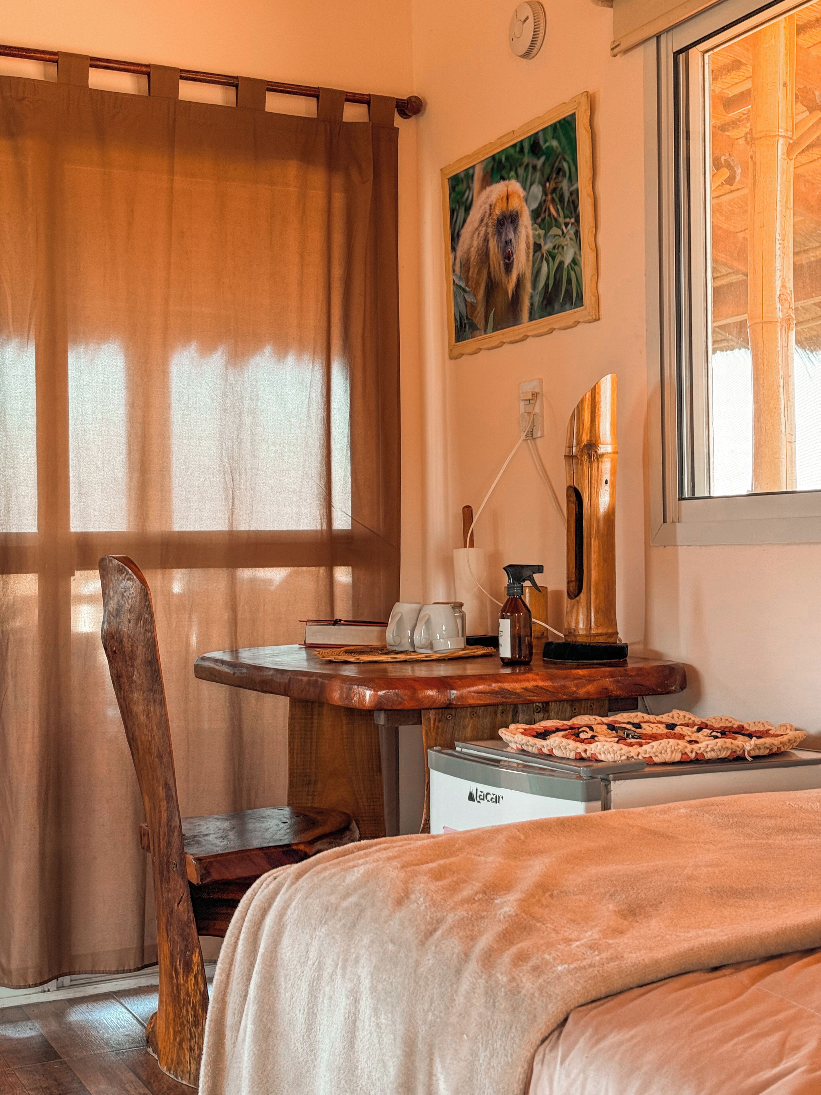 Habitació amb escriptori de fusta, cadira, llit, quadre i finestra amb cortines.