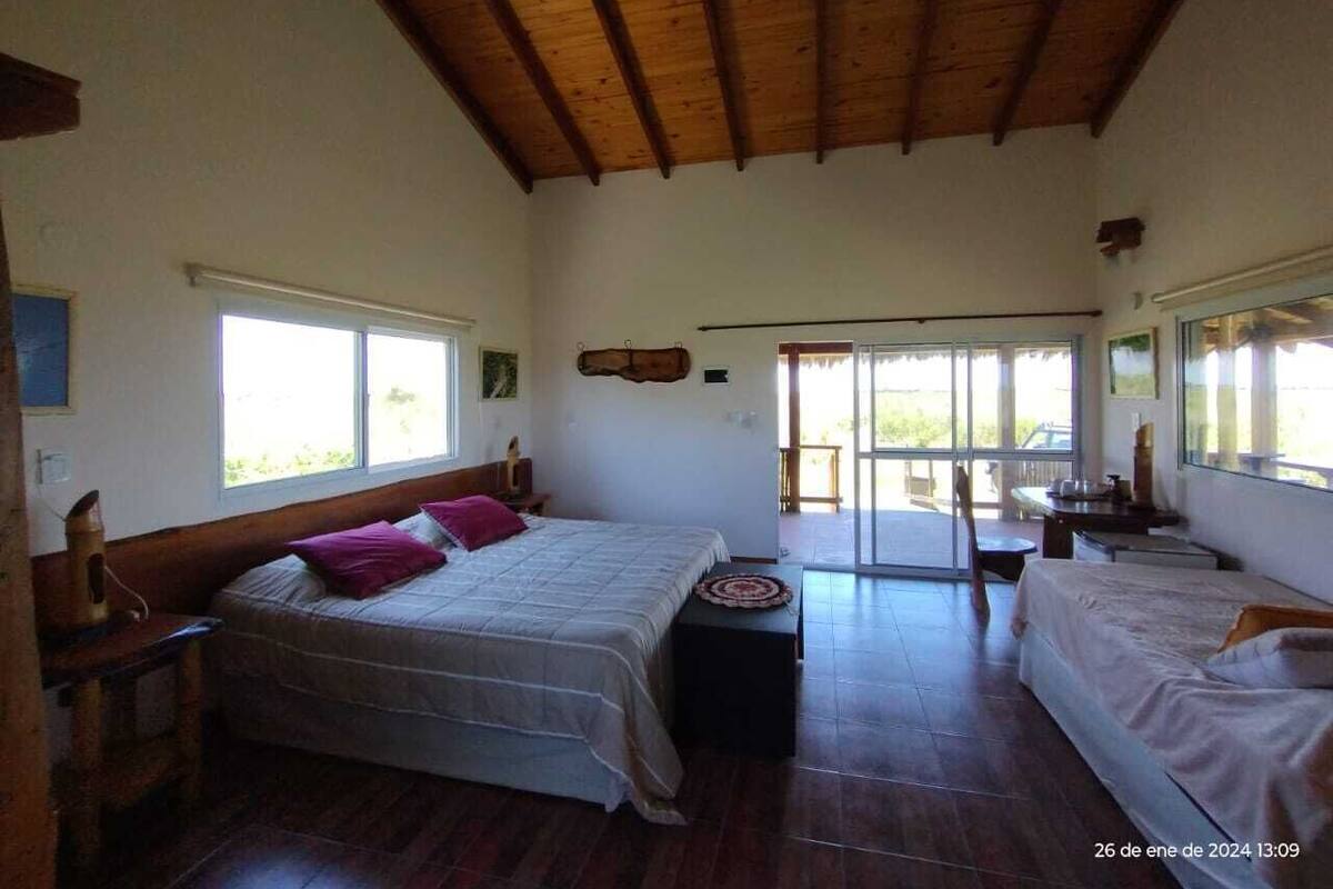 A bedroom with two beds, a wooden ceiling, a large window, and a balcony.