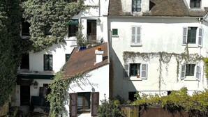 A row of white buildings with green shutters, some with ivy, under a partly cloudy sky. - L'appartement Poulbot (Paris)