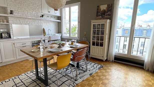 A dining area with a wooden table, chairs, and a white cabinet with glass doors. - L'appartement Poulbot (Paris)