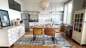 A modern kitchen with white cabinets, a wooden dining table, and a patterned rug. - L'appartement Poulbot (Paris)