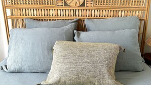 A bed with a woven headboard, multiple pillows, and a textured bedspread. - L'appartement Poulbot (Paris)