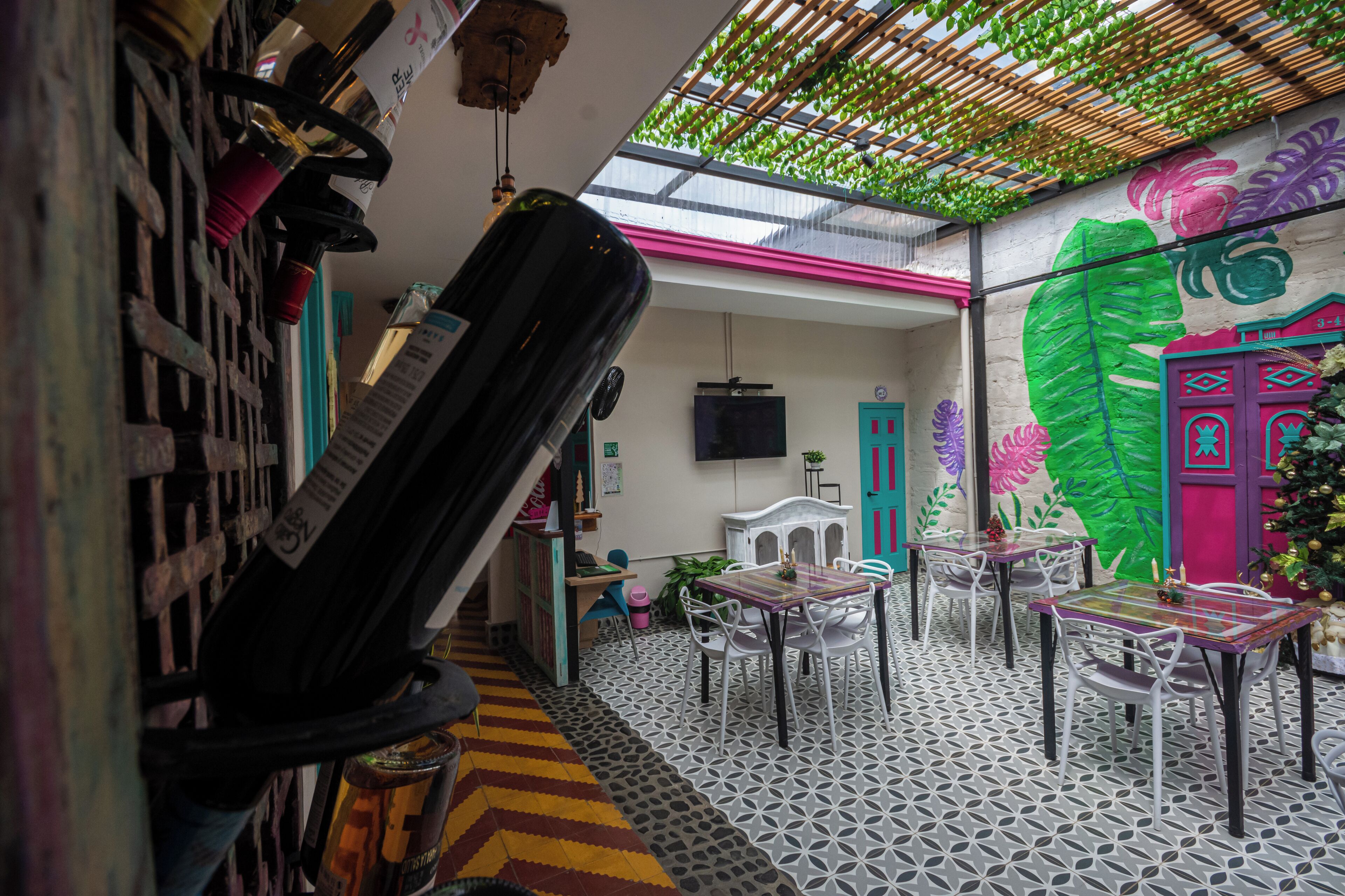 Een restaurant met een unieke geometrische tegelvloer, een groot groen bladerdak en levendige muurkunst.