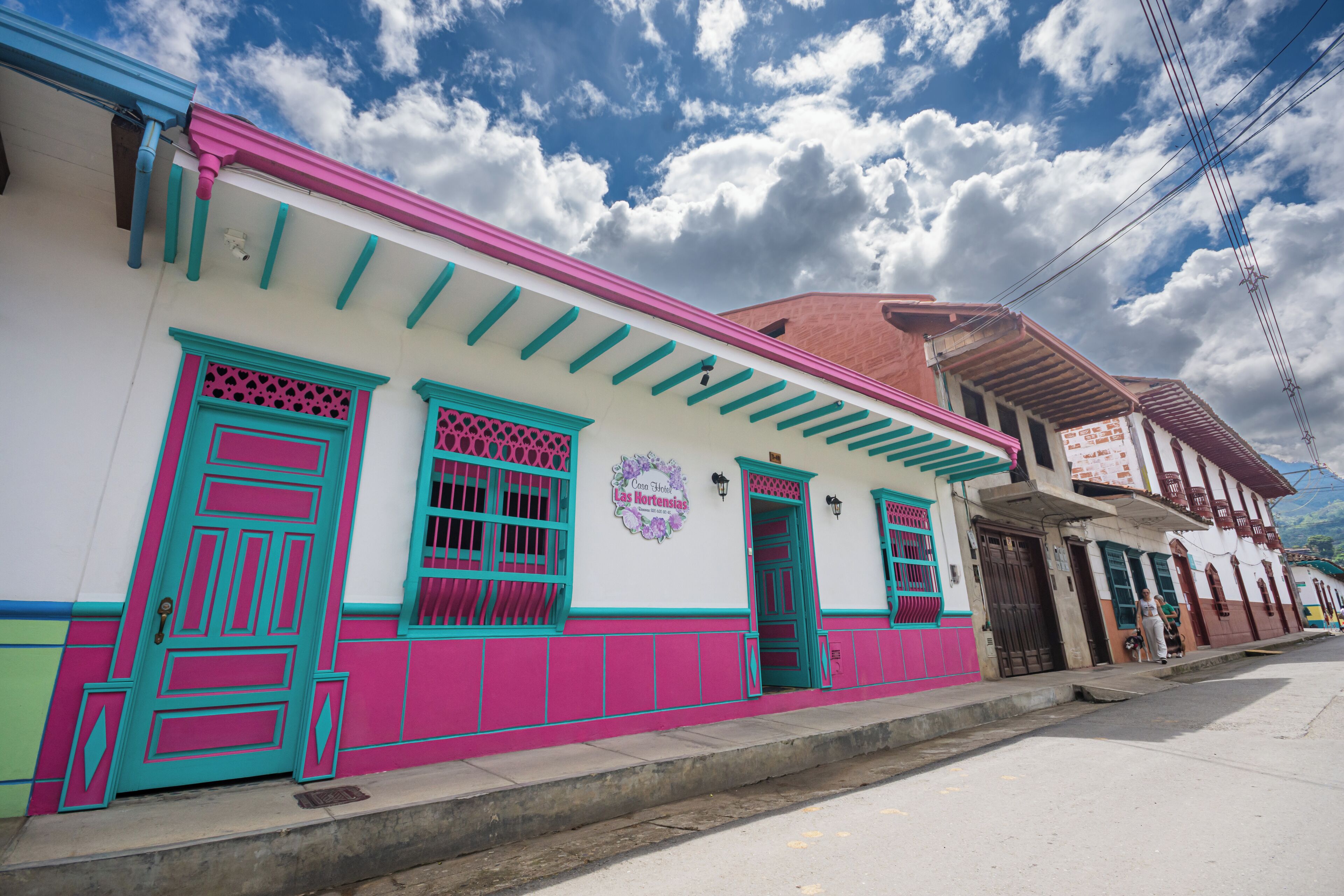 A building with a pink and white facade, green window frames, and a sign that reads "Comite de Fiestas Las Hortas."