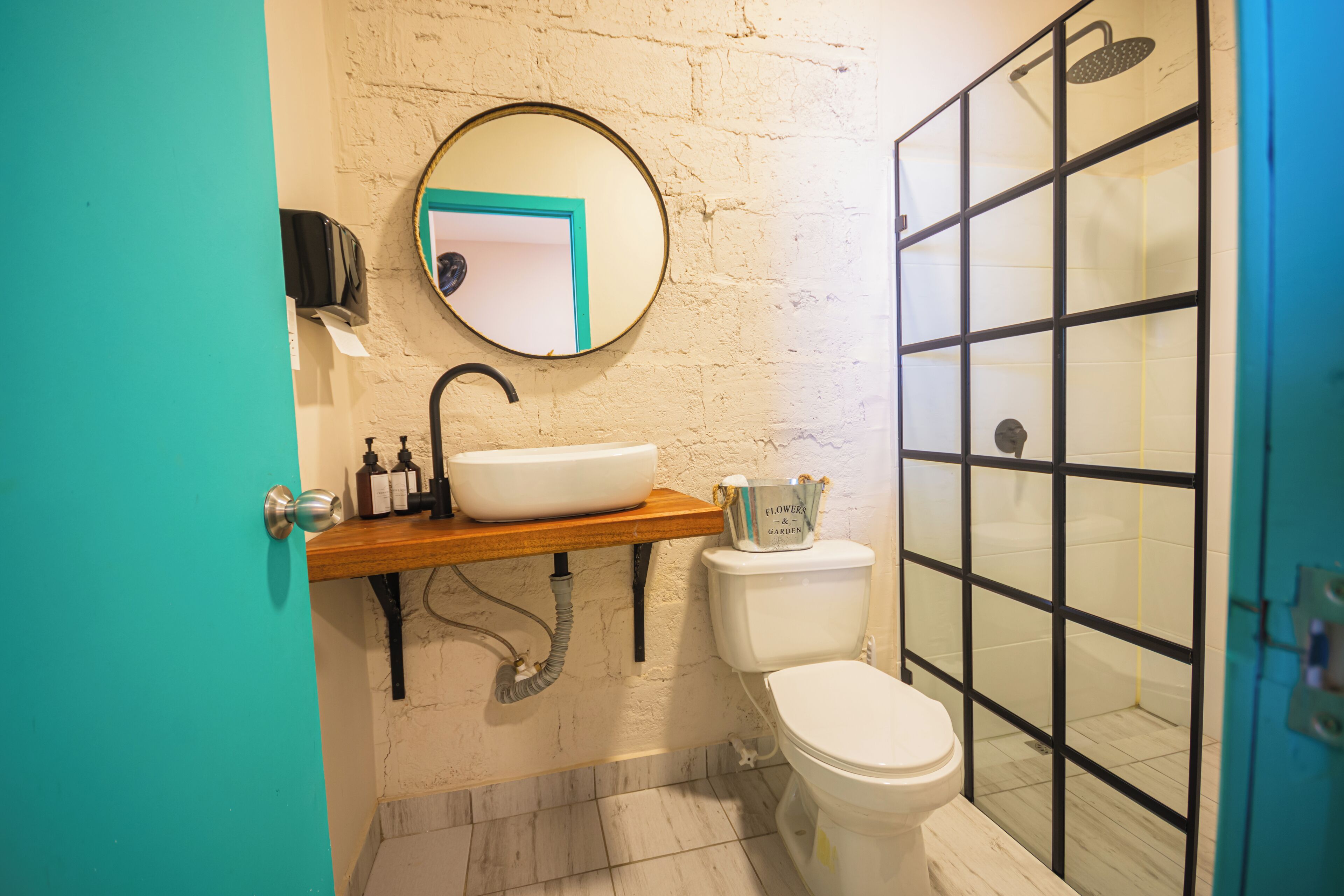 Un baño con tocador de madera, espejo redondo, inodoro y ducha con mampara de vidrio.