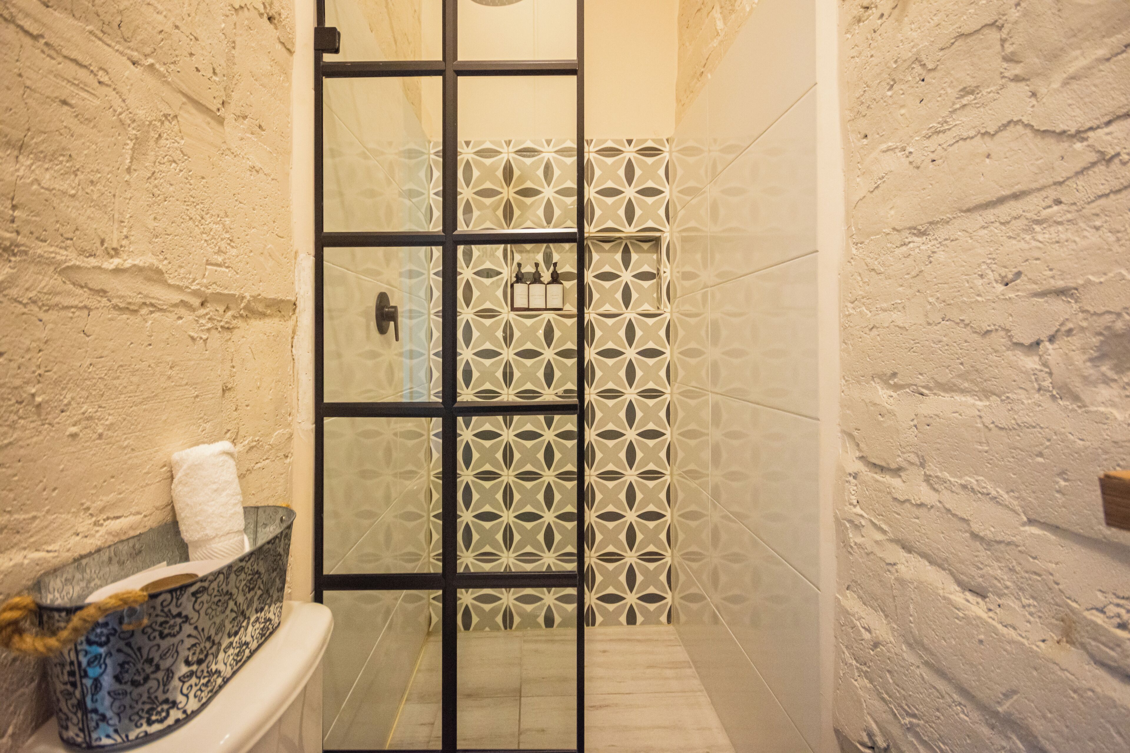 A bathroom with a white bathtub, a glass shower enclosure, and a patterned wall.
