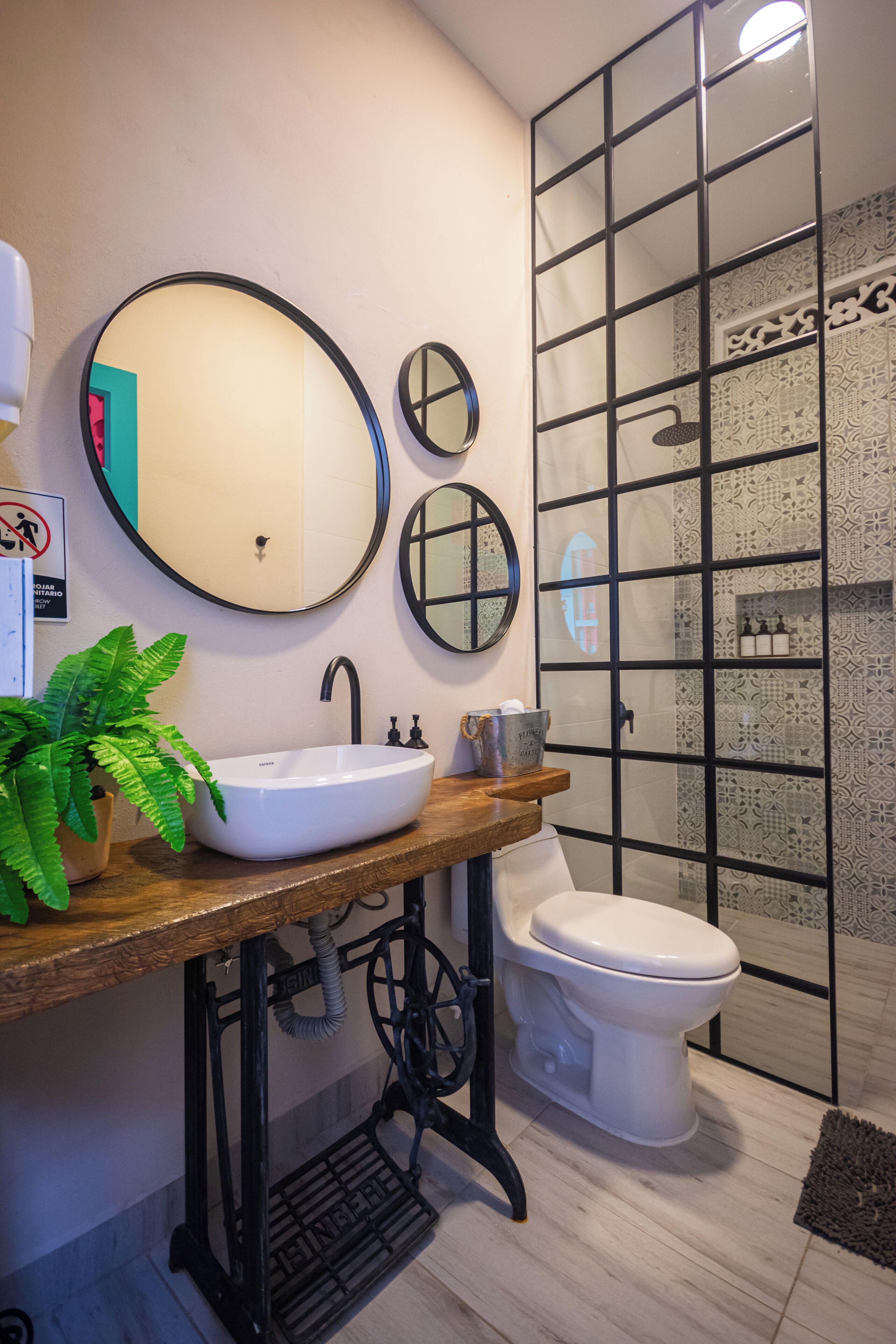 A bathroom with a white sink, two mirrors, a toilet, and a shower area with patterned tiles.