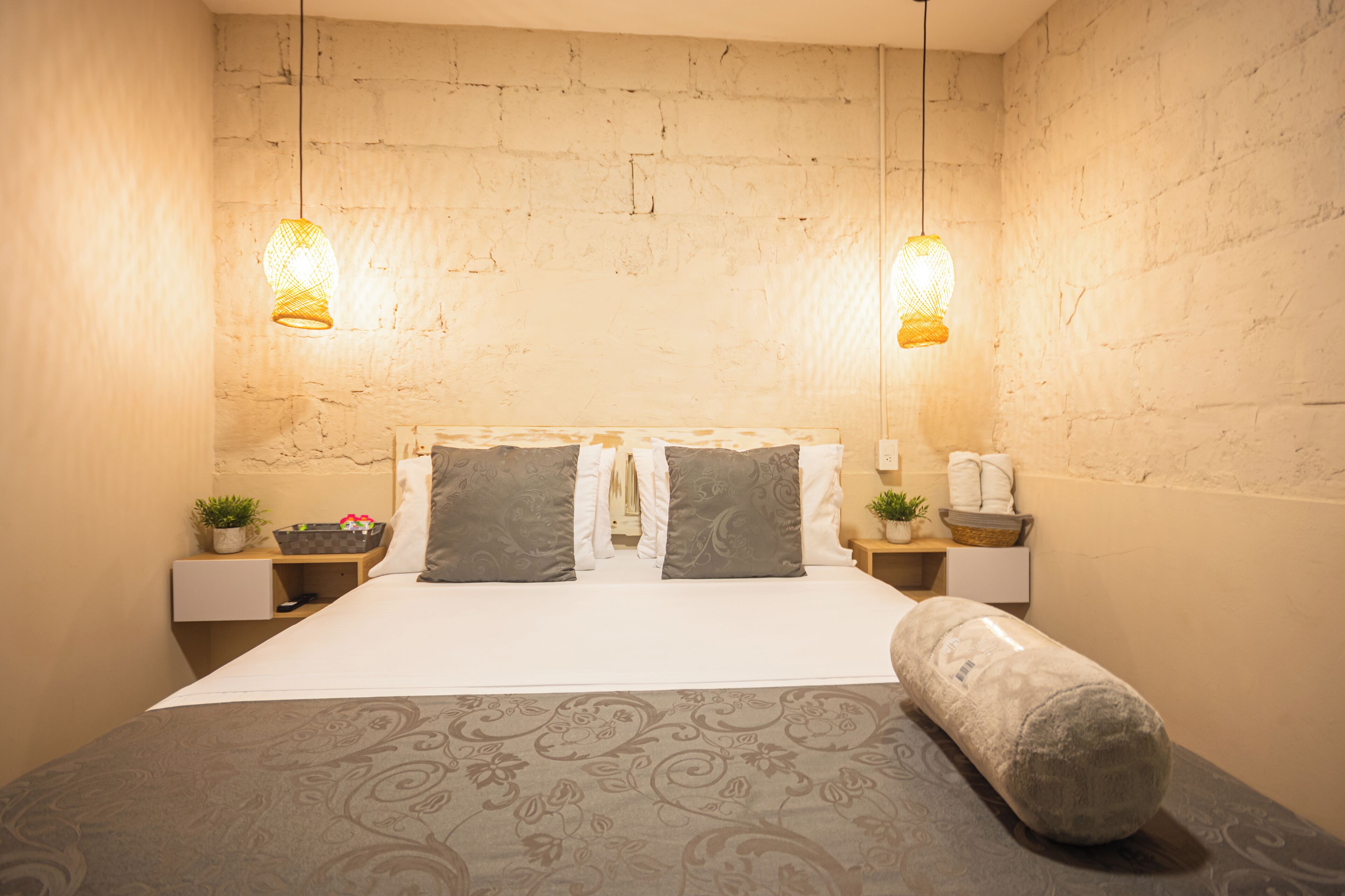 A neatly made bed with a patterned bedspread, two bedside tables with lamps, and a brick wall.