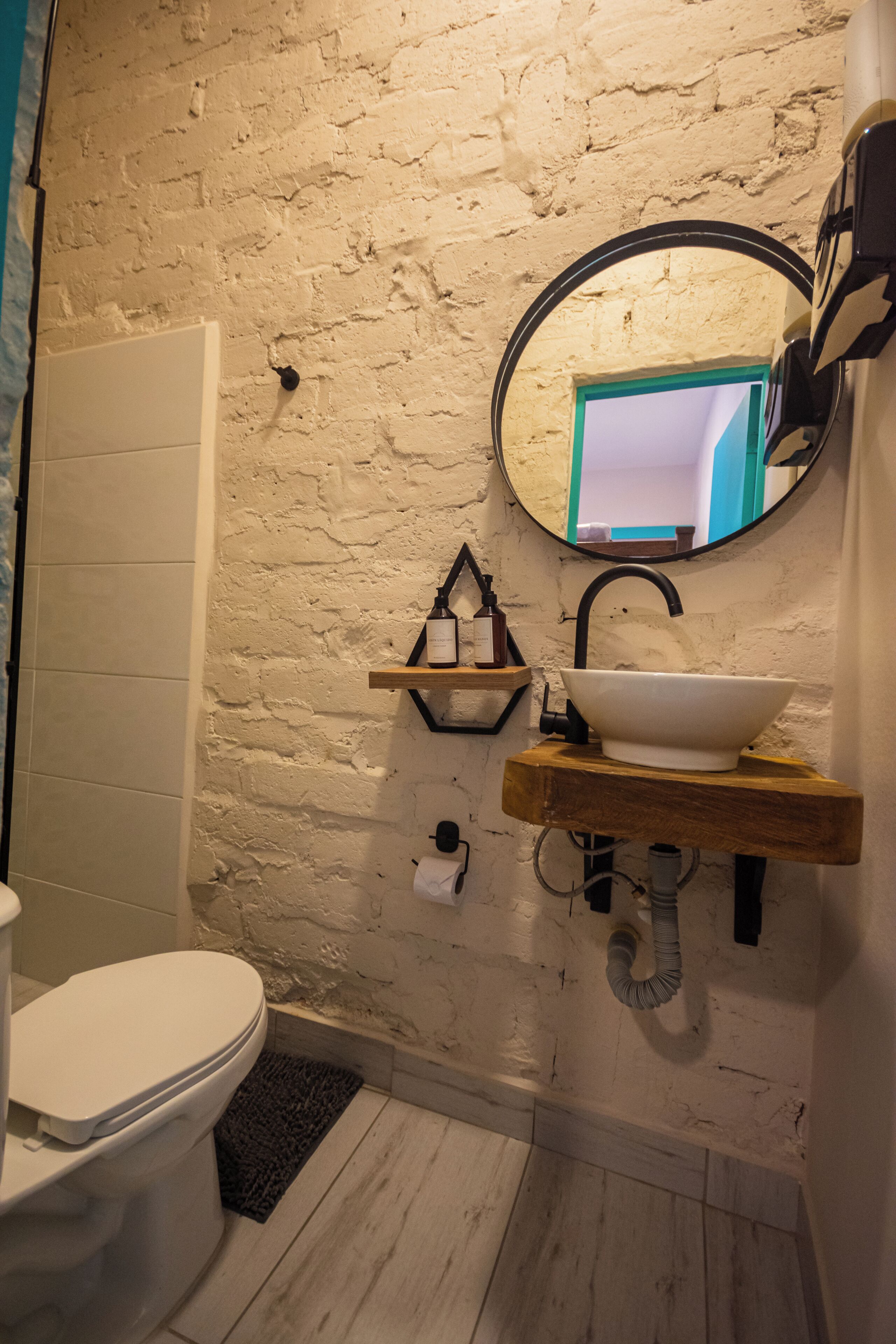 A bathroom with a white toilet, a wooden sink, a round mirror, and a brick wall.