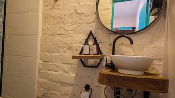 A bathroom with a white toilet, a wooden sink, a round mirror, and a brick wall.
