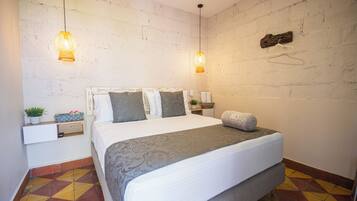 A bedroom with a bed, two bedside tables, a hanging light fixture, and a brick wall.