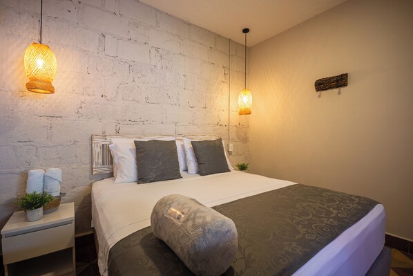 A neatly made bed with a patterned bedspread, a bedside table with a plant, and two wall-mounted lamps.