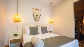 A neatly made bed with a patterned bedspread, two bedside lamps, a wall-mounted macrame decoration, and a small bedside plant. - CASA HOTEL LAS HORTENSIAS (Jardin)