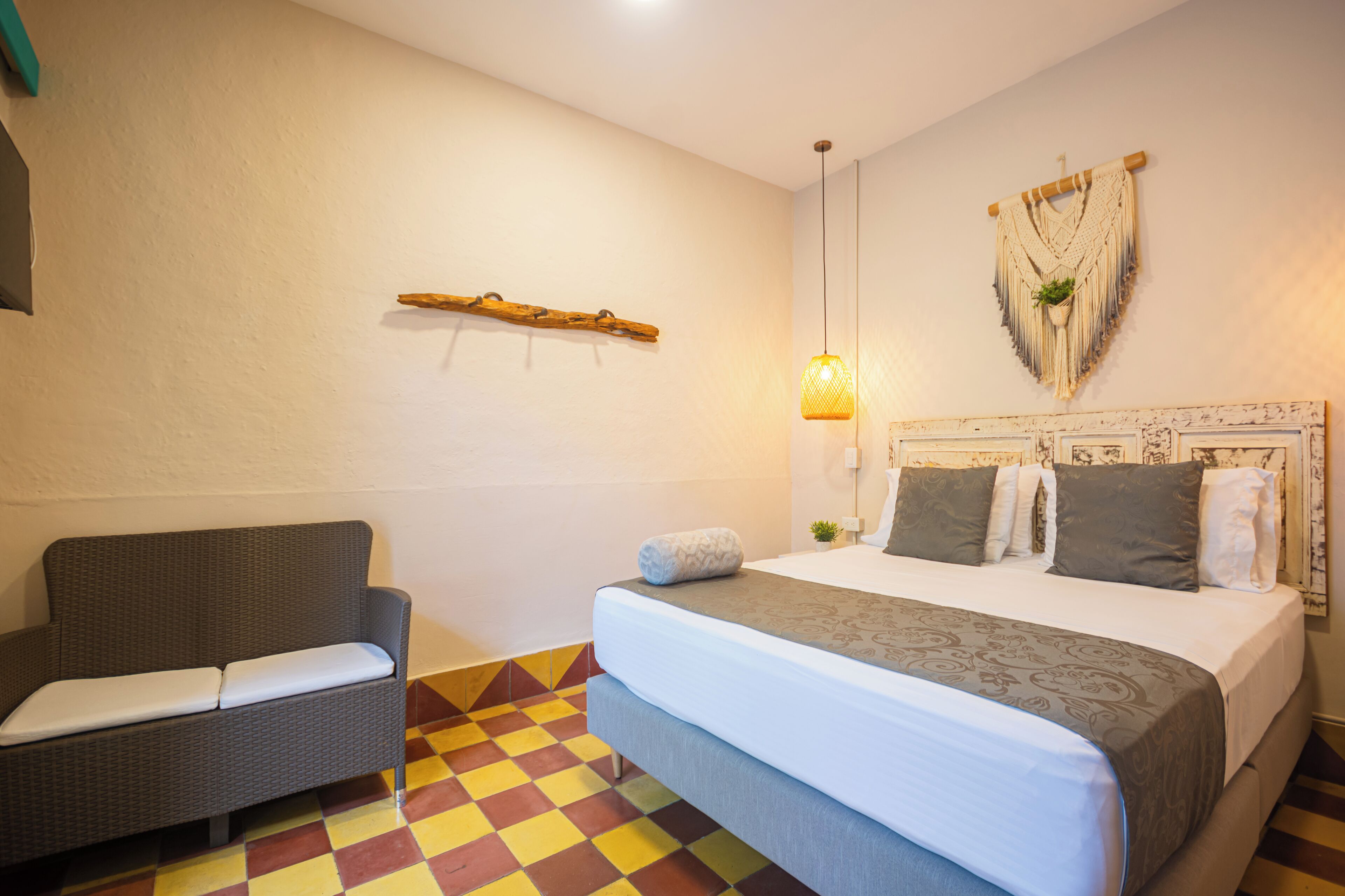 Une chambre avec un lit, un canapé, une décoration murale en macramé et une petite plante.
