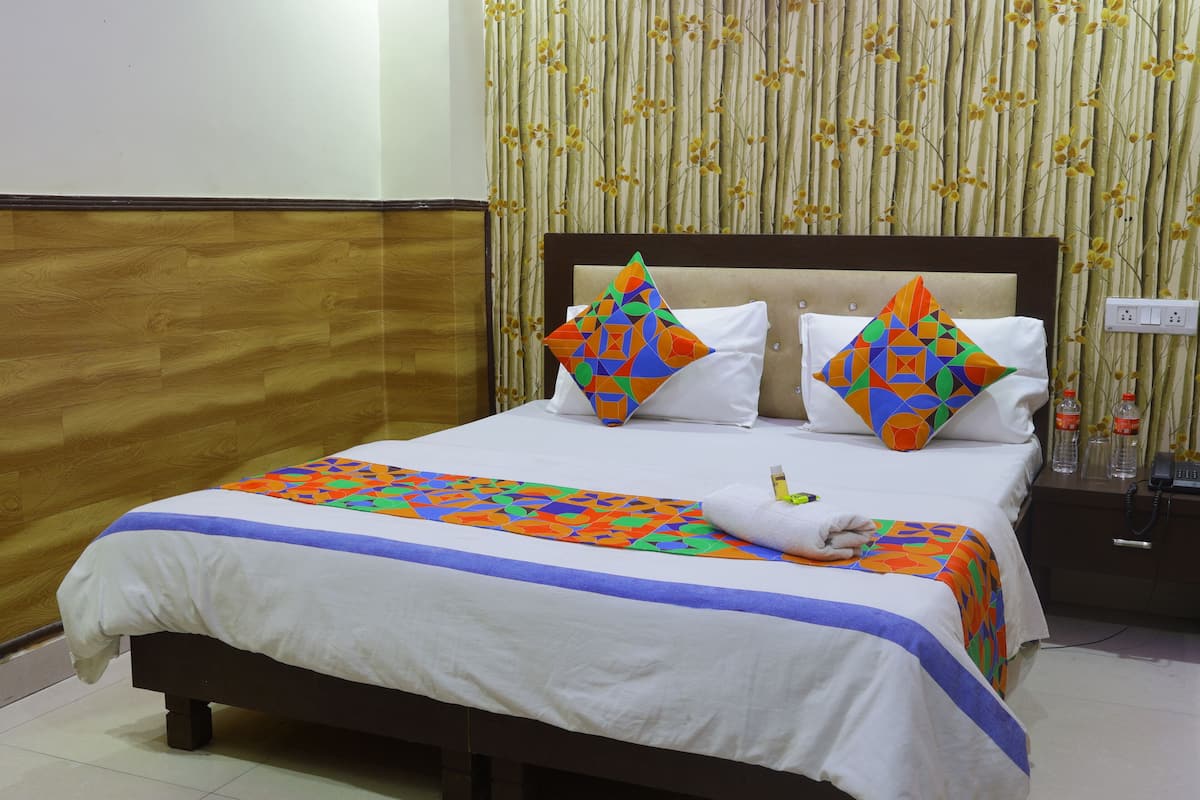 A neatly made bed with a colorful geometric-patterned bedspread and pillows, a wooden headboard, and a nightstand with a phone and bottles.