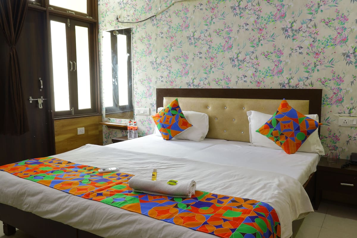 A hotel room with a bed, floral wallpaper, and a window with curtains.
