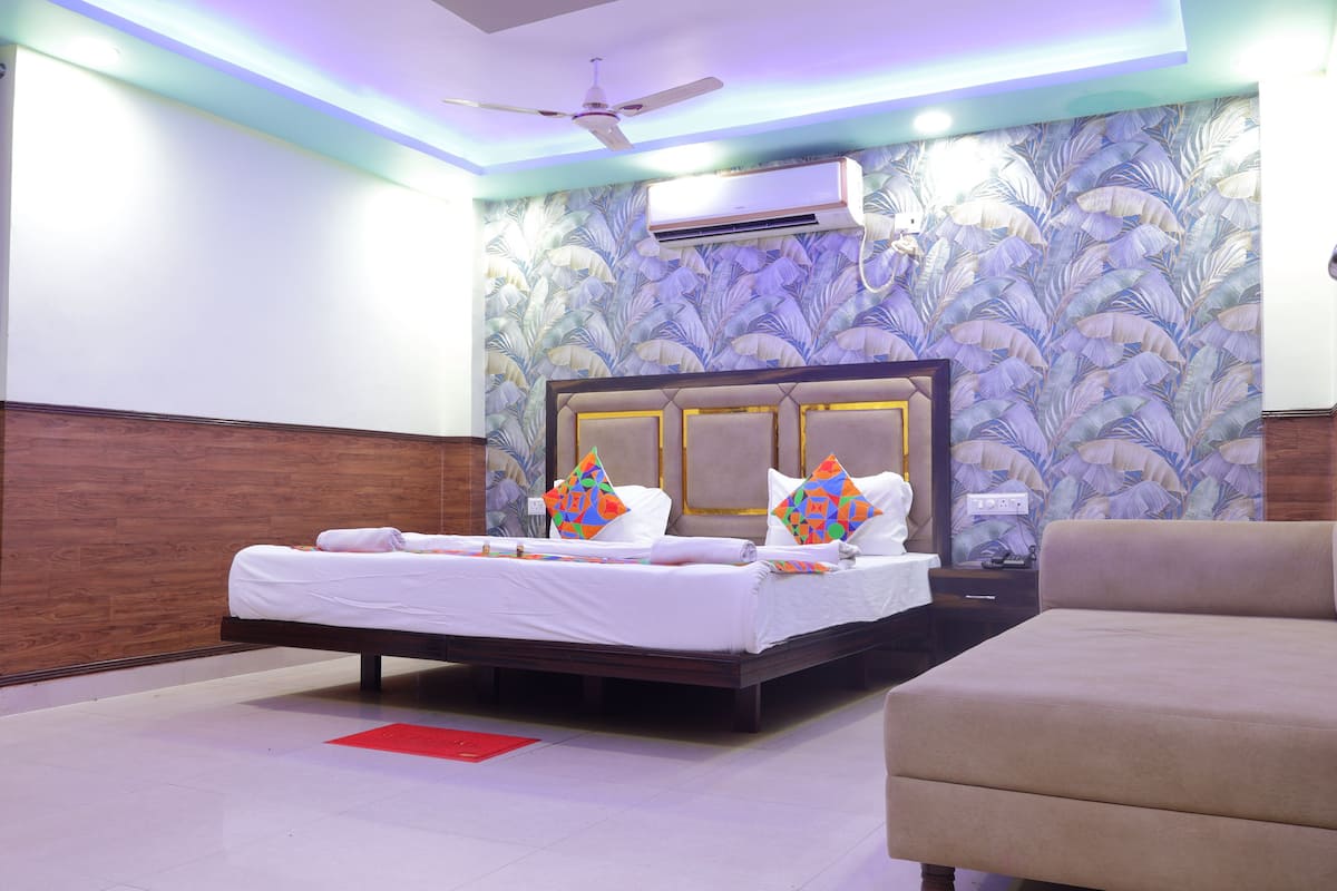 A hotel room with a bed, a sofa, an air conditioning unit, and a ceiling fan.